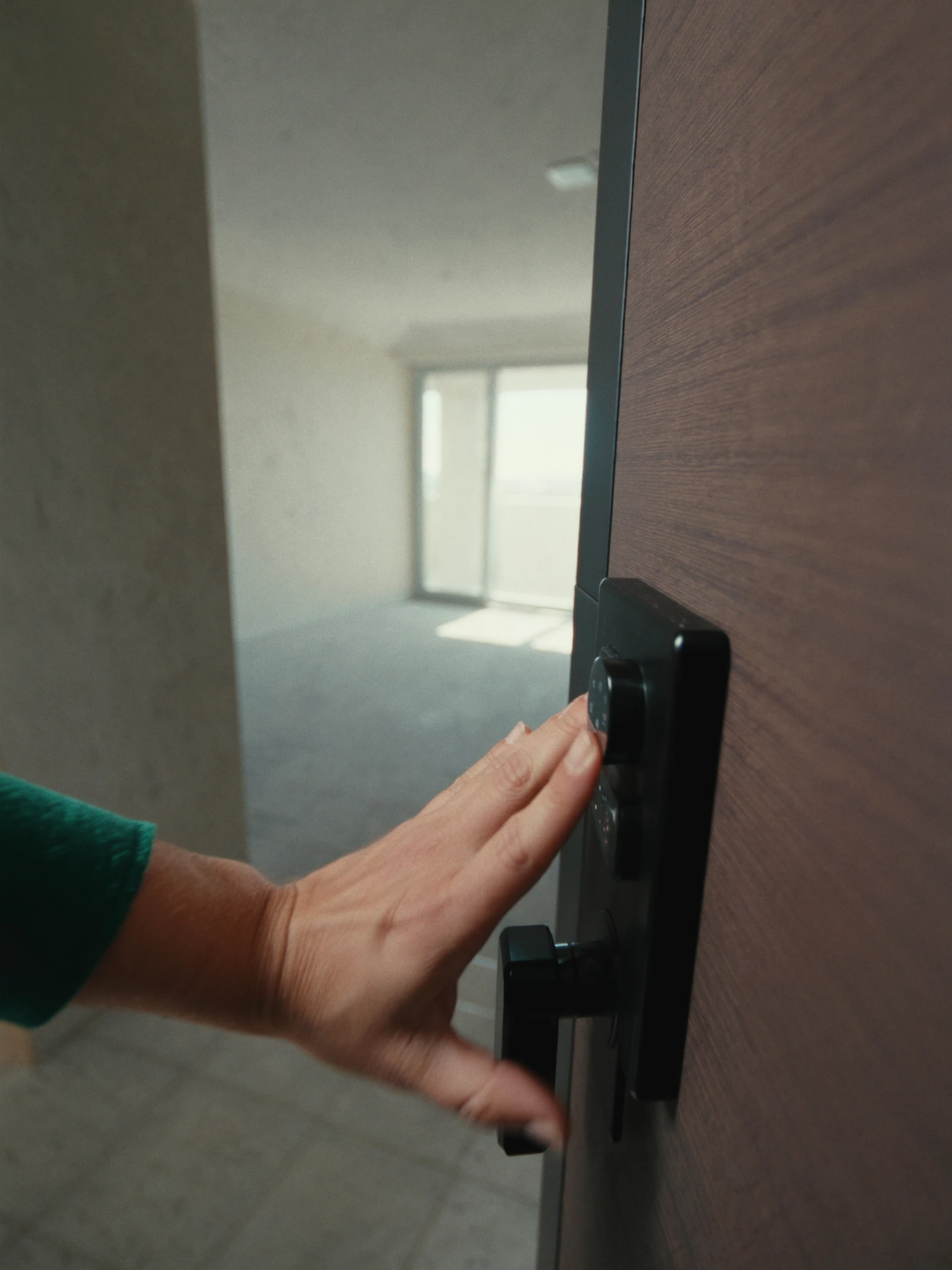 A tenant's hand opens a unit door with a smart lock, onto an empty sunlit apartment.
